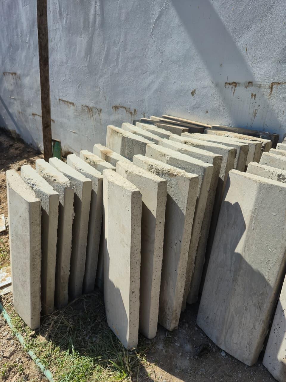 Rows of flat grey slabs stood on edge and leaning against a whitewashed wall, packed close together with the rough cast edges facing out.