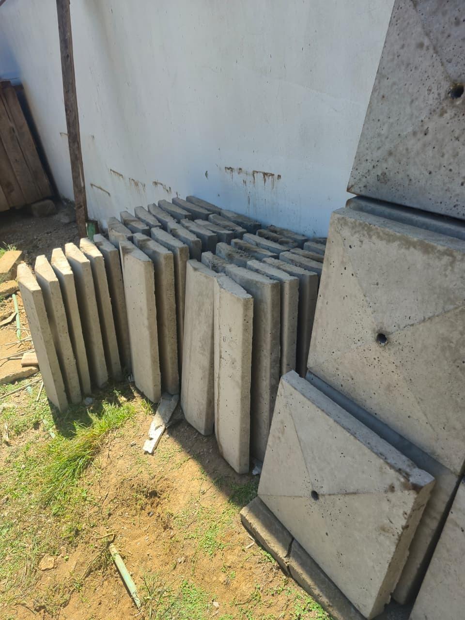 Pillar caps stacked on edge in a long row beside a whitewashed wall, with two finished caps laid flat in the foreground showing the pyramid face and the centre hole.
