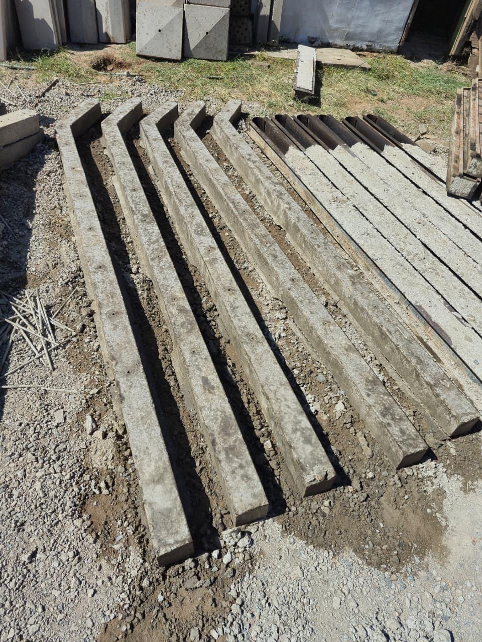 Seven square-section posts laid out parallel on the ground to cure, tie wire offcuts to one side and the steel casting moulds still lying alongside them.