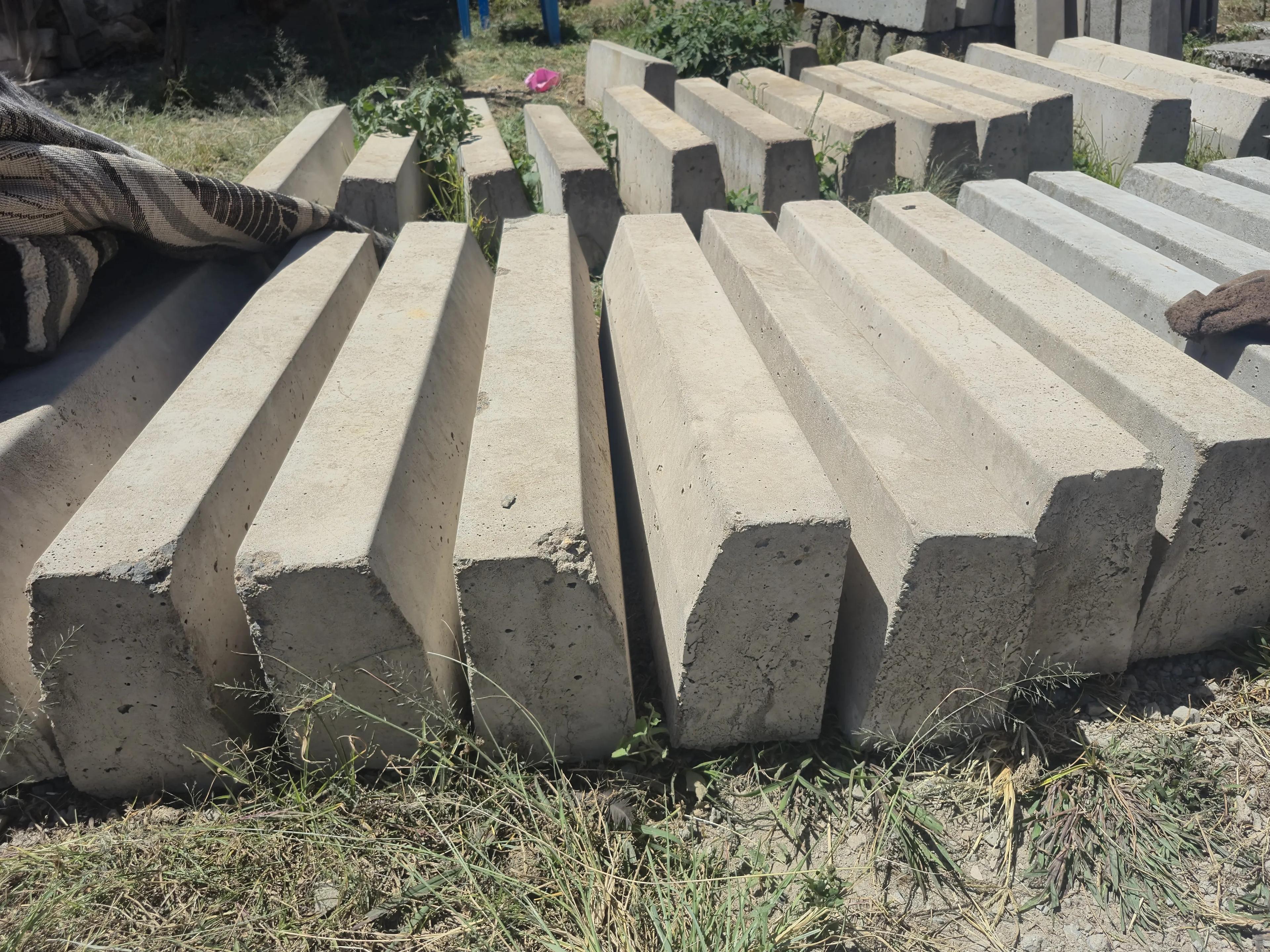 Heavy chamfered road kerbs laid out in rows on the grass, the angled top edge running the length of each one and further rows stacked behind.